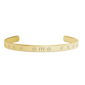 May include: Gold bangle bracelet with a clover design and the number 777 engraved on the front.