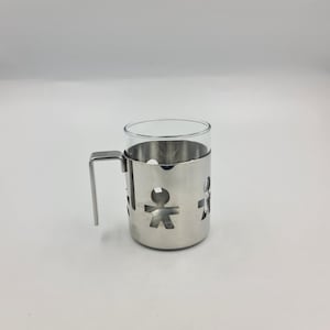 Peut inclure: Une tasse en verre transparent avec un support en acier inoxydable. Le support présente des découpes de silhouettes humaines et une poignée. La tasse est conçue pour contenir une petite quantité de liquide.