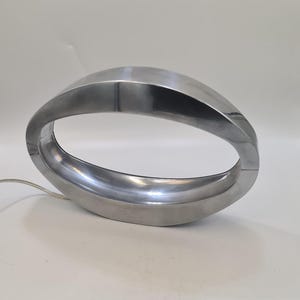 May include: A silver, oval-shaped table lamp with a smooth, curved design. The lamp has a cord and a light bulb.