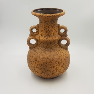 Puede incluir: Un jarrón de cerámica marrón moteado con una base ancha y un borde acampanado. El jarrón presenta cuatro asas de bucle y una superficie texturizada, adecuado para la decoración del hogar.