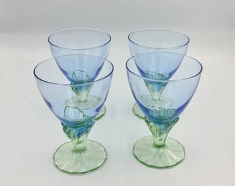Könnte beinhalten: Ein Set aus vier Stielgläsern mit hellblauen Kelchen und blassgrünen Füßen. Jedes Glas besitzt einen markanten, blütenförmigen Stiel, der den Kelch mit einem gewellten, runden Fuß verbindet und so ein einheitliches Bild dieser Gläserserie ergibt.