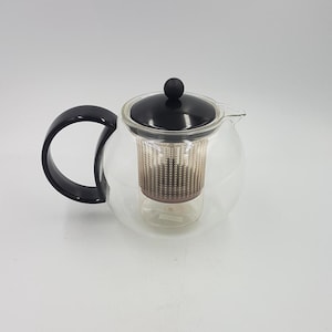 May include: A clear glass teapot with a black lid and handle. The teapot has a built-in strainer for loose leaf tea.