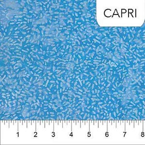 May include: Close-up of a blue fabric with a speckled pattern and a ruler along the bottom edge. The fabric has a light blue background with white, oblong shapes scattered across it. The word "CAPRI" is in a white box in the upper right corner. The ruler measures up to 8 inches.