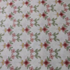 Puede incluir: Tela blanca con un patrón repetido de flores rosas, hojas verdes y cruces rojas. El texto "Graceful Moments" está impreso en la parte inferior de la tela.