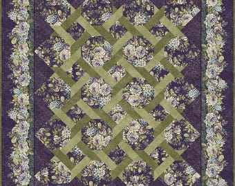 Puede incluir: Una colcha rectangular con un patrón central de cuadrados de tela floral de color morado oscuro superpuestos con una red de tiras de tela verde oliva. La colcha está enmarcada por un borde ancho de racimos florales blancos, morados y verdes.