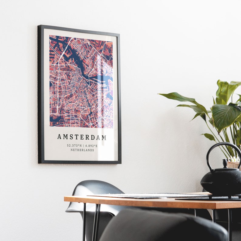 May include: A black framed print of a map of Amsterdam, Netherlands. The map is in shades of red and blue. The text "AMSTERDAM" is at the bottom of the print, along with the coordinates "52.3733&deg;N | 4.8932&deg;E".