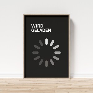 Könnte beinhalten: Ein gerahmtes Poster mit schwarzem Hintergrund zeigt den deutschen Text "WIRD GELADEN" in Weiß, über einem kreisförmigen Ladesymbol. Das Ladesymbol besteht aus weißen und grauen Segmenten. Der Rahmen hat eine helle Holzfarbe.