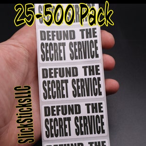 May include: A hand holds a stack of white rectangular stickers with black text. The stickers read "DEFUND THE SECRET SERVICE." The text "25-500 Pack" is in yellow at the top, and "SlickSticksLLC" is in yellow on the side.