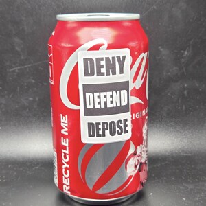 K&ouml;nnte beinhalten: Eine rote Aluminiumdose mit einem wei&szlig;en Etikett, auf dem "Recycle Me" steht. Ein wei&szlig;er Aufkleber mit schwarzem Text, auf dem "Deny Defend Depose" steht, ist an der Dose angebracht.