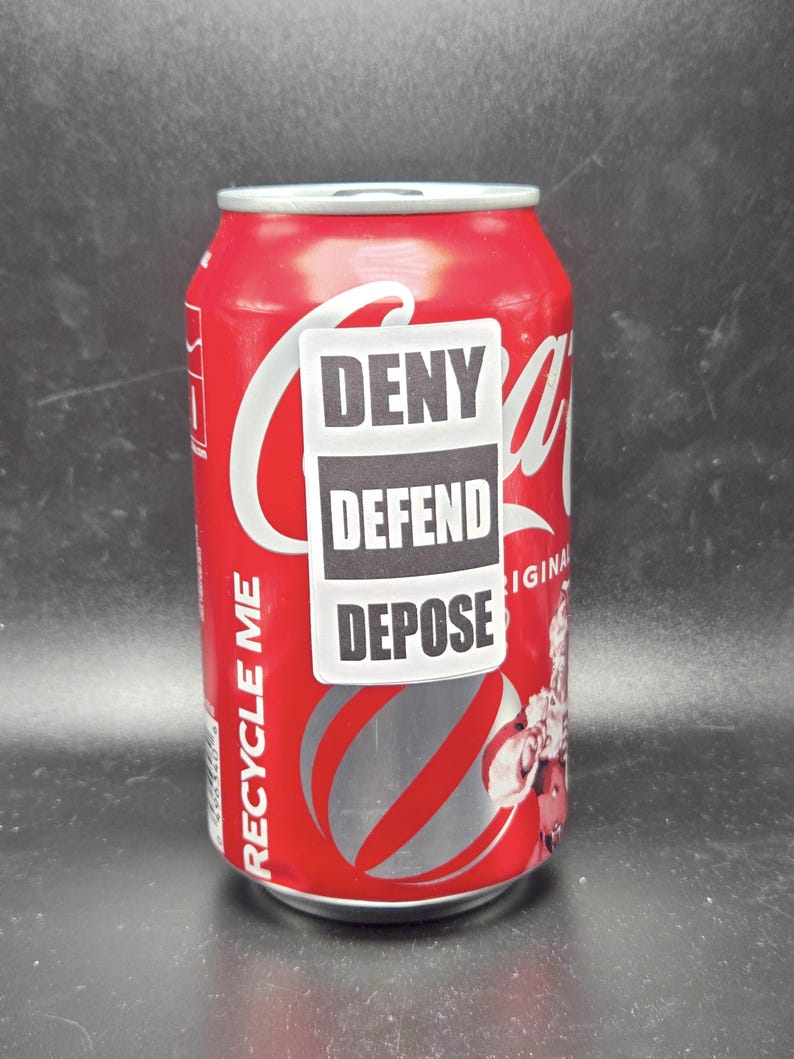 K&ouml;nnte beinhalten: Eine rote Aluminiumdose mit einem wei&szlig;en Etikett, auf dem "Recycle Me" steht. Ein wei&szlig;er Aufkleber mit schwarzem Text, auf dem "Deny Defend Depose" steht, ist an der Dose angebracht.