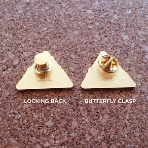 May include: Two gold-coloured triangular pins with different backings. The pin on the left has a locking back and the pin on the right has a butterfly clasp. Both pins have the text "K1118" on the back.