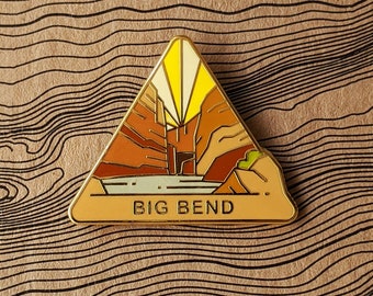 May include: A triangular enamel pin with a depiction of Big Bend National Park in Texas. The pin features a stylized image of a canyon with a river running through it, and the text "BIG BEND" at the bottom.