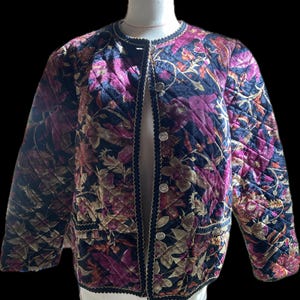 Könnte beinhalten: Eine gesteppte Jacke mit einem floralen Muster in den Farben Pink, Gold und Schwarz. Die Jacke hat einen schwarzen Samtbesatz und silberne Knöpfe.