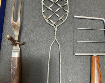 Colección de tres piezas de cocina vintage para servir que consta de un cortador de pasteles, un tenedor para carne con soporte y un colador de metal exclusivo.