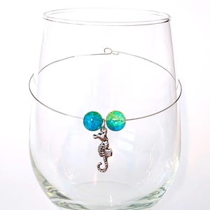 May include: A glass wine charm with a silver seahorse charm and two green and blue glass beads.