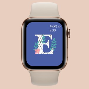 May include: A rose gold Apple Watch with a cream-colored band displays a blue screen with the letter "E" in white polka dots, adorned with floral and leaf accents. The time, 8:30, and the day, Mon 10, are also visible.