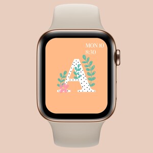 May include: A gold Apple Watch with a white band displays a watch face with a peach background, a black and white polka dot letter A, and green leaves. The time is 8:30 and the date is MON 10.