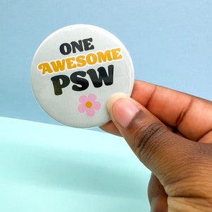 May include: A white button with a pink flower and the text "ONE AWESOME PSW" in black and yellow lettering.