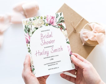 Pode incluir: Um convite de chá de panela branco com uma borda floral de aquarela rosa. O texto diz "Join us for a Bridal Shower in honor of Hailey Smith, sábado, 17 de abril de 2022, 1 PM, 1234 Winterberry Street, Brampton, ON, RSVP até 10 de abril."