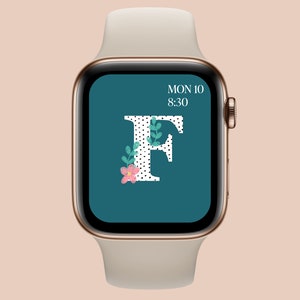 May include: A gold Apple Watch with a white band displays a teal watch face with a white letter "F" with black polka dots and a pink flower and green leaves. The time is 8:30 and the date is MON 10.