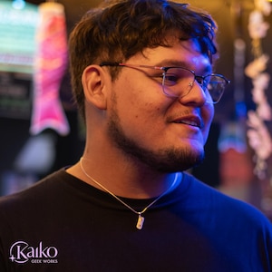 May include: A person wearing eyeglasses and a black t-shirt, with a silver necklace. The image is lit with blue and yellow light. The logo "Kaiko Geek Works" is visible in the bottom left corner.