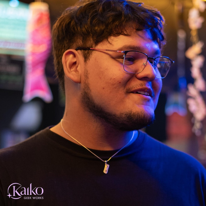 May include: A person wearing eyeglasses and a black t-shirt, with a silver necklace. The image is lit with blue and yellow light. The logo "Kaiko Geek Works" is visible in the bottom left corner.