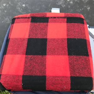 Puede incluir: Manta de lana roja y negra a cuadros con una etiqueta blanca en la parte superior.