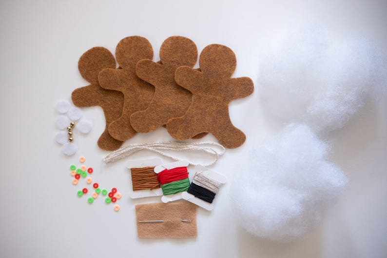 May include: A craft kit with brown felt gingerbread man shapes, white stuffing, spools of thread, beads, and a needle. The kit includes various craft supplies for creating handmade decorations or ornaments.