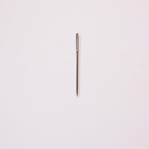 May include: A single, silver sewing needle with a small eye and a sharp point, centered on a white background. The needle is a common tool used for hand sewing and crafting projects.