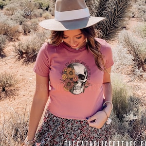 May include: A pink t-shirt with a skull and floral design. The text on the shirt reads "and to dust you shall return".
