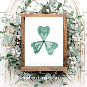 May include: A watercolour illustration of a shamrock with the words "Father", "Son", and "Holy Spirit" written on each leaf. The shamrock is green and white and is framed in a brown wooden frame.