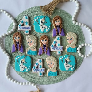 These 12 delicious cookies are decorated with designs inspired by Frozen&#39;s characters, including Olaf, Elsa, Ana, and a birthday number