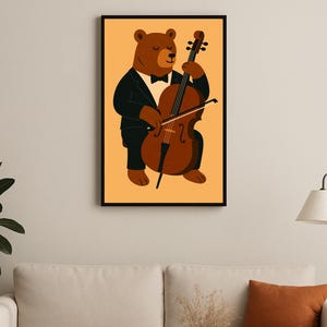 Può includere: Una stampa artistica incorniciata raffigurante un orso bruno che suona il violoncello. L'orso indossa uno smoking nero con papillon. Il violoncello è marrone, su sfondo arancione chiaro.