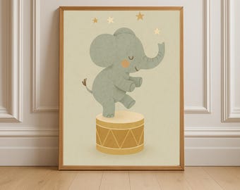 May include: A framed print featuring a whimsical illustration of a gray elephant balancing on a yellow drum. The elephant has a peach-colored cheek and is surrounded by gold stars. The artwork is set against a light beige background.