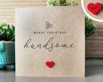 May include: A brown card with the text "Merry Christmas Handsome" and a small red heart button. The card has a small holly design in the top left corner.
