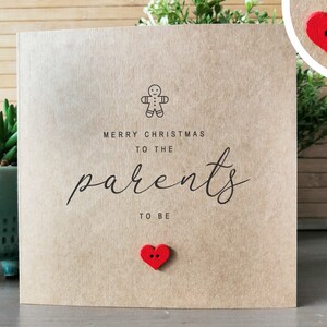May include: A brown card with the text "Merry Christmas to the parents to be" and a gingerbread man icon. There is a red heart button on the card.