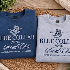 Puede incluir: Una sudadera azul marino y una sudadera gris jaspeado, ambas con texto bordado que dice "EST. OT BLUE COLLAR WIVES Social Club UNITED BY LONG SHIFTS & LATE DINNERS" y una ilustración de un par de botas de trabajo.