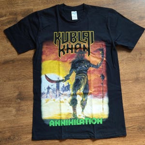 Könnte beinhalten: Schwarzes T-Shirt mit einem Grafikdruck eines Kriegers, der ein Schwert hält. Die Grafik ist in Gelb, Orange und Grün. Der Text "Kublai Khan" und "Annihilation" ist auf dem T-Shirt aufgedruckt.