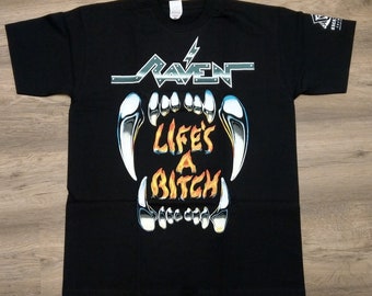 Könnte beinhalten: Schwarzes T-Shirt mit einem Grafikdruck von einer Reihe scharfer Zähne und dem Text "Raven" und "Life's a Bitch" in einer feurigen orangefarbenen Schrift.