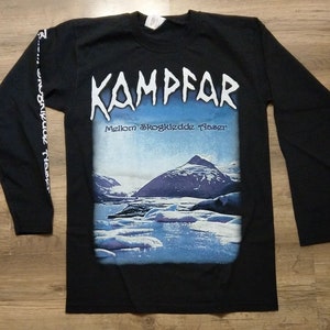 Op de afbeelding: Zwart langarm T-shirt met een grafische print van een bergketen en een wateroppervlak. De tekst "KAMPFAR" en "Mellom Skogkledde Fjell" staat op het shirt gedrukt.