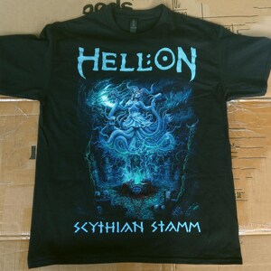 Puede incluir: Camiseta negra con un gráfico azul. La palabra "HELL:ON" está encima de una ilustración de una figura con cabello suelto y una forma de serpiente. El texto "SCYTHIAN STAMM" está debajo.
