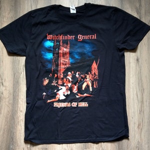 Op de afbeelding: Zwart T-shirt met een grafische print van een kerk 's nachts met mensen ervoor. De tekst "Witchfinder General" en "Friends of Hell" staat op het shirt gedrukt.
