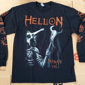 Puede incluir: Camiseta negra de manga larga con un estampado gráfico naranja de una figura esquelética sosteniendo un bastón con un cráneo en la parte superior. El texto "HELLION" y "SHAMAN" están impresos en naranja en la camiseta.