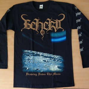 Puede incluir: Camiseta negra de manga larga con un gráfico de la luna y el nombre de la banda "Behemoth" en una fuente estilizada. El texto "Drawing Down The Moon" está impreso debajo del gráfico.