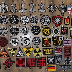 Könnte beinhalten: Eine Sammlung von 63 Bügelbildern mit verschiedenen Designs, darunter Symbole, Logos und Text. Die Bügelbilder sind in Reihen auf einer Holzoberfläche angeordnet. Einige der Designs beinhalten einen Schädel, einen Wolf, einen Dreizack, ein Peace-Zeichen, ein Kreuz, einen Pentagramm und ein Biohazard-Symbol. Die Bügelbilder sind in verschiedenen Farben, darunter Schwarz, Weiß, Rot, Blau und Grün.