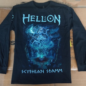 Puede incluir: Camiseta negra de manga larga con la palabra "HELL:ON" en azul claro, sobre un gráfico detallado en azul y turquesa. El gráfico representa una figura con tentáculos arremolinados y el texto "SCYTHIAN STAMM" en azul claro debajo.