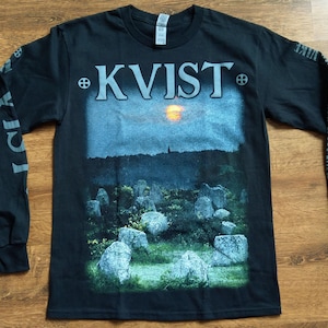 Op de afbeelding: Zwart langarm T-shirt met een grafische print van een zonsondergang boven een veld met staande stenen. De tekst "KVIST" is in wit op de voorkant van het shirt gedrukt.