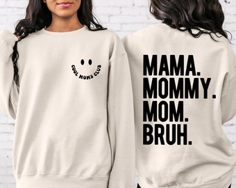 May include: A cream-coloured sweatshirt with the text "COOL MOMS CLUB" and a smiley face on the front. The back of the sweatshirt has the text "MAMA. MOMMY. MOM. BRUH."