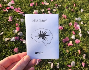 Può includere: Un biglietto bianco con la parola "Migraine" e un'illustrazione in bianco e nero di un cervello con una stella al suo interno. La parola "Brain" è stampata sotto l'illustrazione.