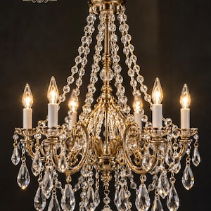 May include: A gold-toned dollhouse chandelier with a 1/12 scale design, featuring multiple arms, white candle-style light covers, and clear crystal-like beads and teardrop-shaped pendants. The text DIY 1/12 SCALE CRYSTAL CHANDELIER FOR DOLLHOUSE is visible.